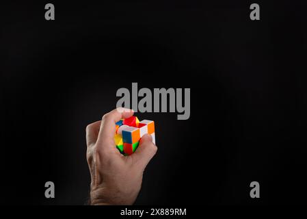 Salvador, Bahia, Brazil - May 15, 2024: Rubiks cube in a persons hands, portrait, black background. Man holding Rubiks cube and playing Stock Photo