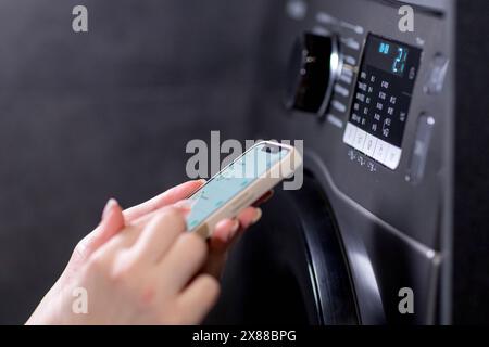 Woman controls washing machine with a phone. Stock Photo