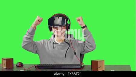 POV of gamer enjoying vr video games sitting at workstation over greenscreen background, playing online with colleagues enjoying rpg gameplay. Young guy using virtual reality glasses. Stock Photo