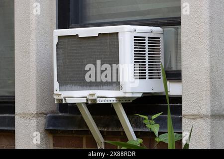 exterior view of air conditioning window unit extruding from the window sill with a portable safety ledge support installed under it Stock Photo