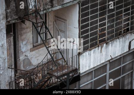 Abandoned Lisbon house with a crumbling facade, featuring rusty fire escapes and broken windows. A pigeon perches on the dilapidated structure, accent Stock Photo