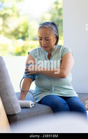 At home, middle-aged Asian female checking blood pressure, wearing a light green top Stock Photo