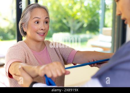 At home, Asian young female nurse and middle-aged patient using resistance bands Stock Photo