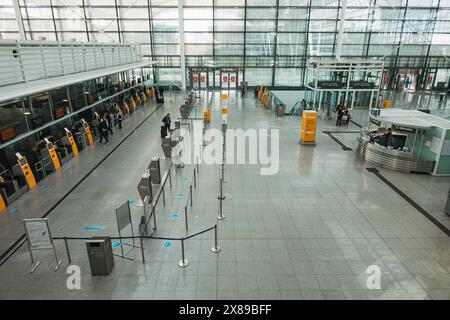 an empty check-in area in Terminal 2 at Munich International Airport, Germany on a quiet afternoon. Walls of windows let plenty of natural light in Stock Photo
