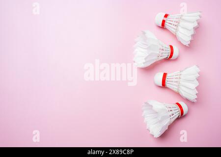 Flat lay of three white badminton shuttlecocks with red details arranged diagonally on a vibrant pink background, providing space for text or design e Stock Photo