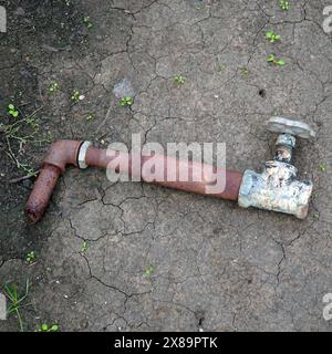A fragment of an old rusty pipe with a tap on the ground Stock Photo