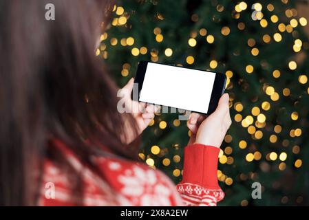 Woman holding smartphone with mock-up screen horizontal position on Christmas bokeh background. Mobile Phone in hand. Close up hands Stock Photo