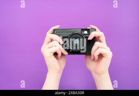 black manual retro camera in hand on a purple background. isolate. banner. Stock Photo