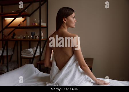 Woman client wrapped in towel sitting on massage table Stock Photo