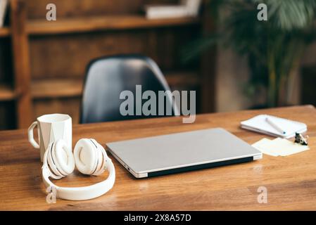 Workplace concept. Silver laptop with cup, headphones and notebook on a wood table in a home interior. Freelance home office Stock Photo