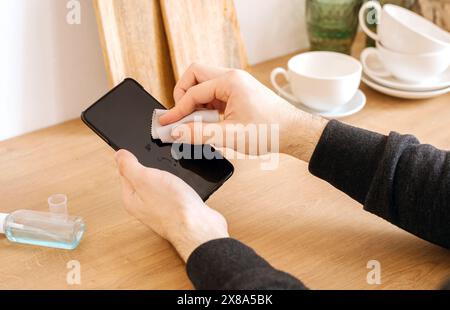 Male hands are cleaning with antiseptic dust and dirt black mobile phone in the kitchen, at home. Stock Photo