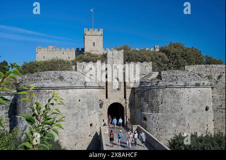 Emery d 'Amboise gate, Rhodes city walls, tourists enter the medieval castle through a large stone gate, massive towers and clear blue sky in the back Stock Photo