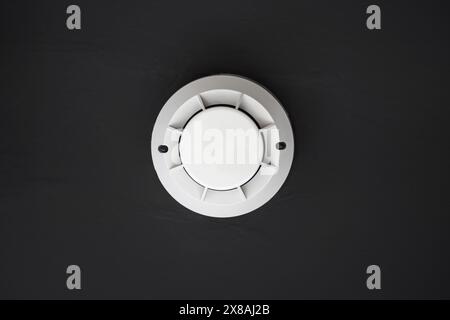 Fire and smoke detector visible from below on black ceiling Stock Photo