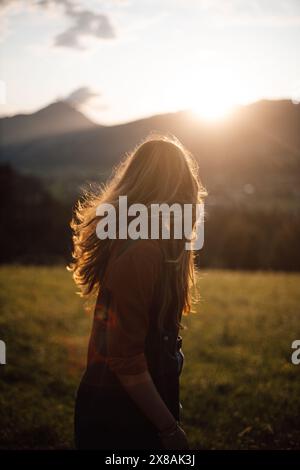 Brunette woman with flowing hair at sunset in meadow with mountains Stock Photo