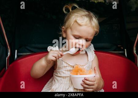 Toddler enthusiastically eating shaved ice in stroller wagon Stock Photo