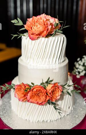 Two-tier white wedding cake with orange roses and green leaves Stock Photo