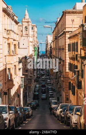 a narrow sloped street in Valletta, Malta, surrounded by apartment buildings made from limestone Stock Photo