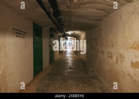 A long, stone tunnel with a green door at the entrance, lit by light from the far end, at the Lascaris War Rooms, Valletta, Malta Stock Photo