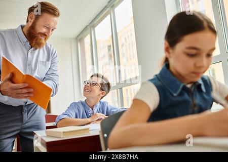 A male teacher stands next to a student in a lively classroom environment, engaging in interactive learning and teaching activities. Stock Photo