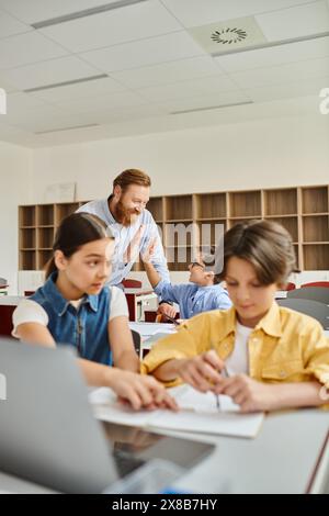 A group of people, including a man teacher, sitting at desks in a bright, lively classroom, engaging in a lesson. Stock Photo