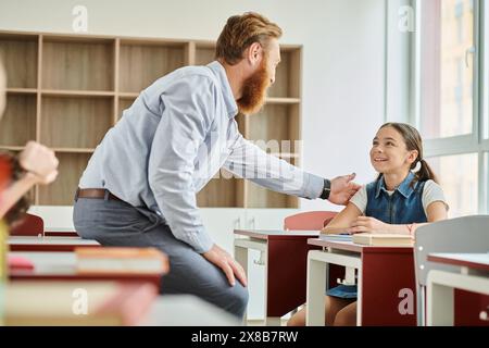 A man teacher encouraging little girl in a colorful, energetic classroom setting. Stock Photo