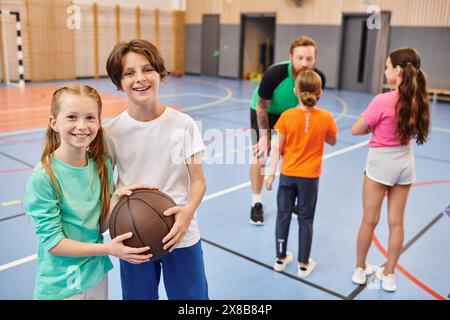 group of kids, including a man teacher, engaging in basketball activities in a gym setting. Stock Photo