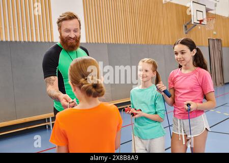 Diverse group of people, including kids and a teacher, standing attentively around each other in a lively gym, the teacher instructing with enthusiasm Stock Photo