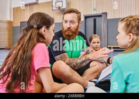 A bearded man sits on a basketball court surrounded by diverse children, engaging them in an inspiring lesson about the game. Stock Photo