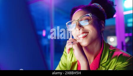 Woman, night and smile in office with neon, tablet and glasses for reading, information technology or coding. Person, girl and developer with click Stock Photo