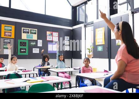 In school, young biracial female teacher is engaging with diverse students in the classroom Stock Photo