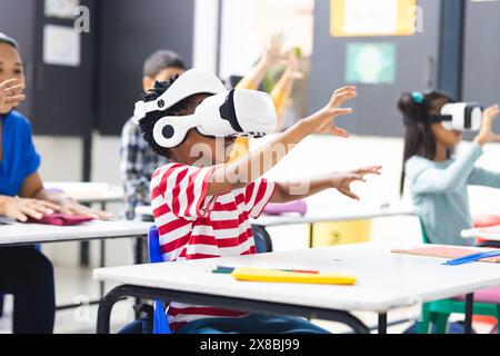 In school, diverse students wearing virtual reality headsets are reaching out in the classroom Stock Photo