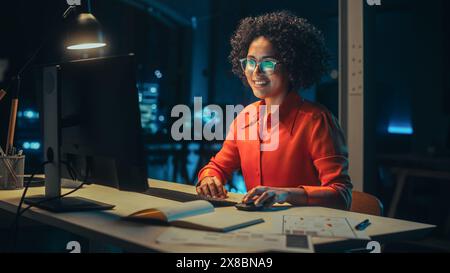 Beautiful Multiethnic Brazilian Female Working on Desktop Computer Late at Night. Young Creative Manager Having Fun in the Office, Chatting with Overseas Business Partners, Answering Emails. Stock Photo