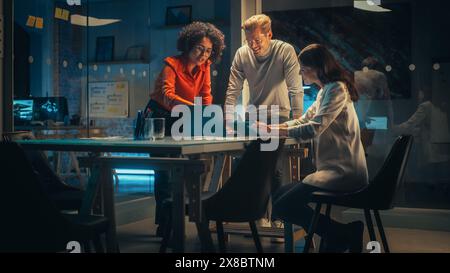 Diverse Team of Young Managers Discussing Work at a Meeting in Office at Night. Successful Business Partners Talking About a Marketing Campaign, Getting Familiar with Company Reports Stock Photo