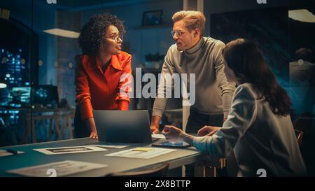 Small Creative Team Meeting in the Evening in Office. Young Project Manager Bringing Her Research Paper, Focused Marketing Director Using Tablet Computer and Discussing the Analysis. Stock Photo