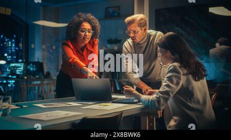 Excited Marketing Manager Leading a Team Meeting in Creative Office Conference Room in the Evening. Confident Multiethnic Female DIscussing a New Project Plan with Agency Employees. Stock Photo