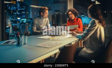Positive Group of Managers Having a Team Meeting Long After Work Hours in the Night. Inspired Colleagues Discussing Annual Financial and Marketing Reports. Teamwork in Creative Office. Stock Photo
