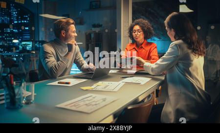 Positive Group of Managers Having a Team Meeting Long After Work Hours in the Night. Inspired Colleagues Discussing Annual Financial and Marketing Reports. Teamwork in Creative Office. Stock Photo