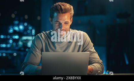 Handsome Man Working on Laptop Computer in a Company Office at Night. Young Specialist Analyzing Reports. Marketing Assistant Developing a Consumer Sales Strategy for a Client. Stock Photo