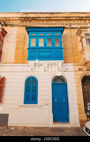 an arched door and gallarija (wooden balcony window) painted a vibrant blue on a limestone house in the town of Sliema, Malta Stock Photo