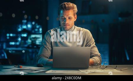 Handsome Man Working on Laptop Computer in a Company Office at Night. Young Specialist Analyzing Reports. Marketing Assistant Developing a Consumer Sales Strategy for a Client. Stock Photo