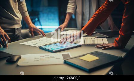 Close Up on Colleagues Discussing a New Business Opportunity, Putting Hands on a Meeting Room Table in an Office at Night. Discussing Project Plan on Tablet Computer with Development Timeline Stock Photo