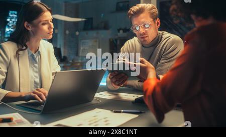 Handsome Software Developer Leading an Office Meeting in Creative Agency Conference Room in the Evening. Multicultural Team Discussing a New Project Plan with Corporate Employees. Stock Photo