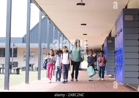 In school, diverse group of students walking with their teacher outdoors Stock Photo
