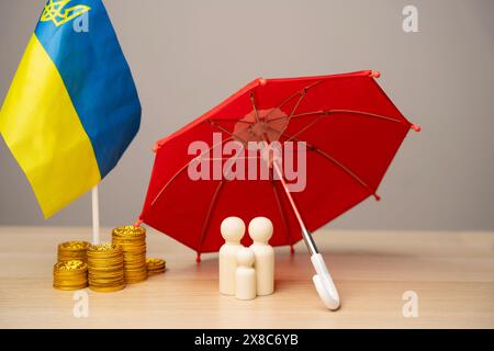 The concept of helping Ukrainian residents affected by the war. Financial support and donation. A married couple stands under an umbrella near coins a Stock Photo