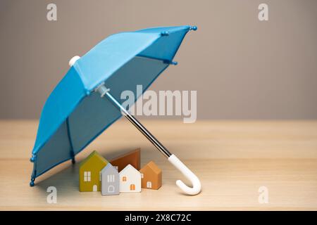 Property and home insurance concept. Wooden houses stand under a blue umbrella. Financial security. Repairs or rebuilding in the event of a covered lo Stock Photo