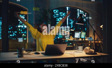 Successful Arab Female Sitting in Creative Agency, Working on Laptop Computer in the Evening. Manager Celebrating Impressive Sales Results. Excited Specialist Happy with Her Project Plan. Stock Photo