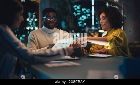 Handsome Software Developer Leading an Office Meeting in Creative Agency Conference Room in the Evening. Multicultural Team Discussing a New Project Plan with Corporate Employees. Stock Photo