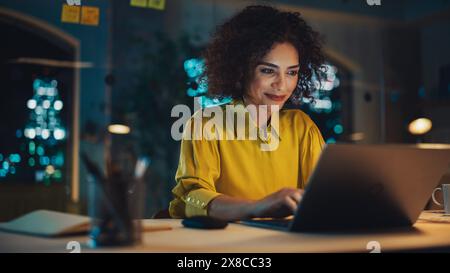 Expressive Multiethnic Middle Eastern Female Working on a Creative Job Position in a Business Agency. Happy Project Manager Browsing Internet, Keeping Important Notes in Notebook. Evening at Work. Stock Photo