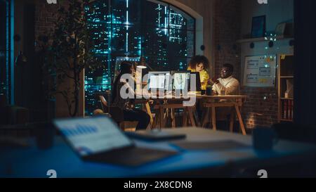 Two Creative Multicultural Colleagues Collaborate on a Project and Work Together as a Team. Marketing Manager and Designer Talking and Discussing Changes to an Advertising Campaign. Evening at Work. Stock Photo
