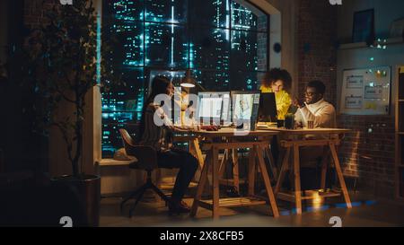 Art Director and Graphic Designer Discussing a Marketing Campaign for Business Partner. Successful Small Diverse Team of Colleagues Working in the Office Together at Night. Stock Photo